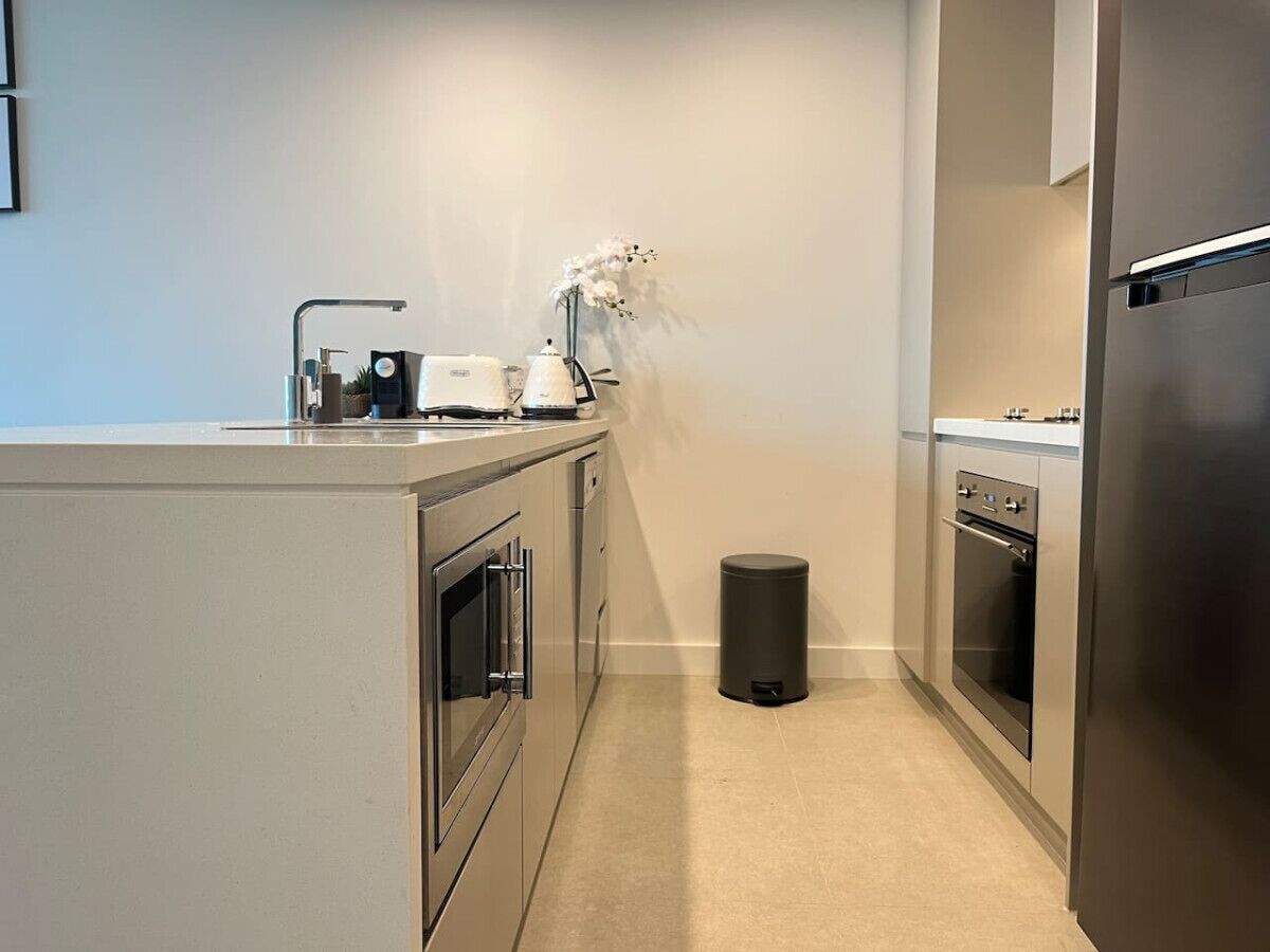 A compact kitchen with stainless steel appliances, a trash bin, and a small countertop.