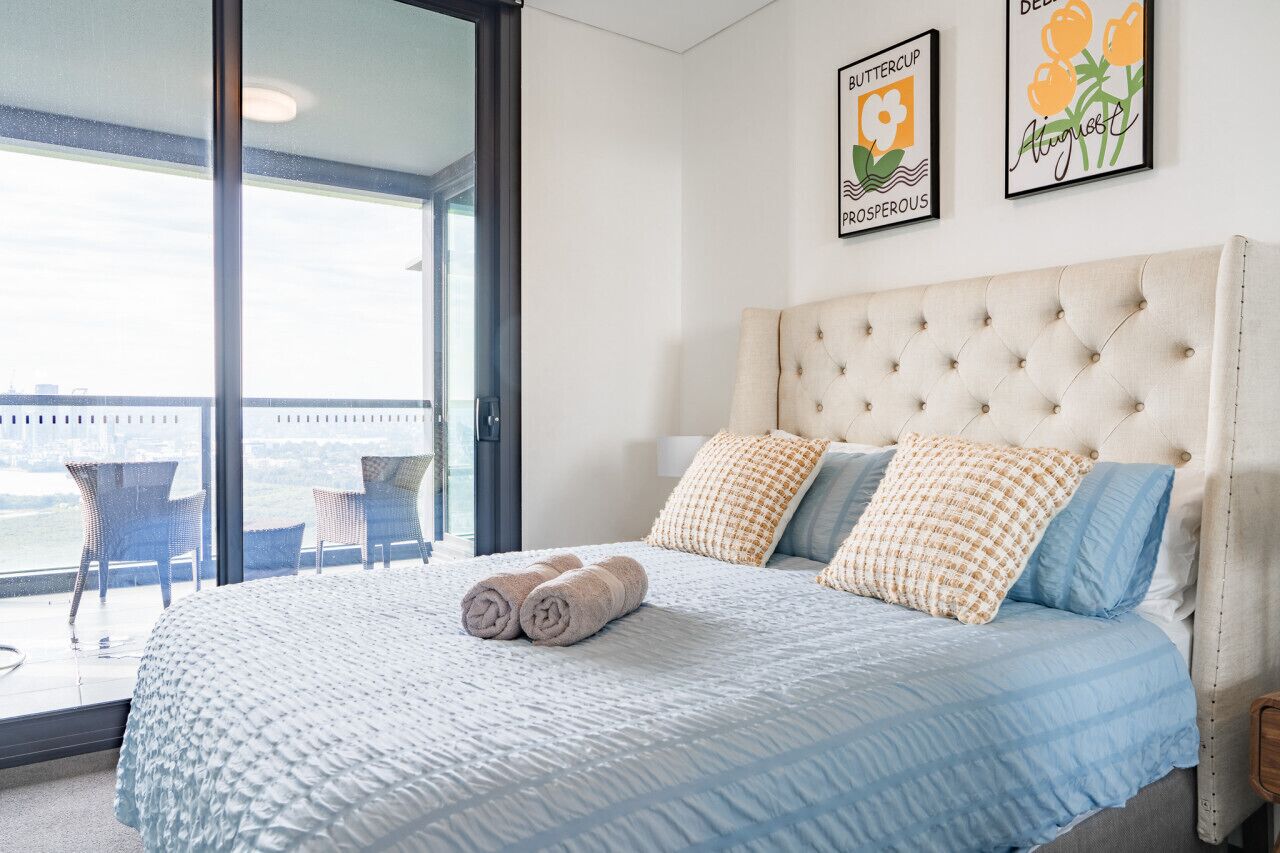 A bedroom with a large bed, two pillows, a view through a glass door, and two framed pictures on the wall.
