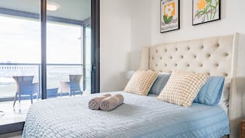A bedroom with a large bed, two pillows, a view through a glass door, and two framed pictures on the wall.