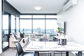 A modern living room with a large window, a dining table, and a sofa.
