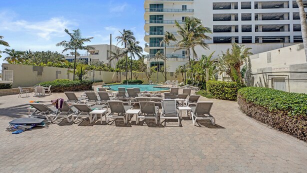A poolside area with lounge chairs and a swimming pool, surrounded by palm trees and a multi-story building. - Haven Beach Gem Condo in Hollywood (Hollywood)