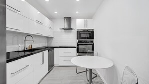 A modern kitchen with white cabinetry, a black countertop, a stainless steel range hood, and a built-in oven. - Haven Beach Gem Condo in Hollywood (Hollywood)