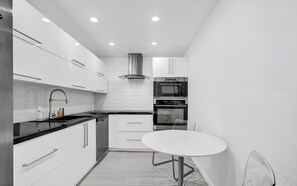 A modern kitchen with white cabinetry, a black countertop, a stainless steel range hood, and a built-in oven. - Haven Beach Gem Condo in Hollywood (Hollywood)