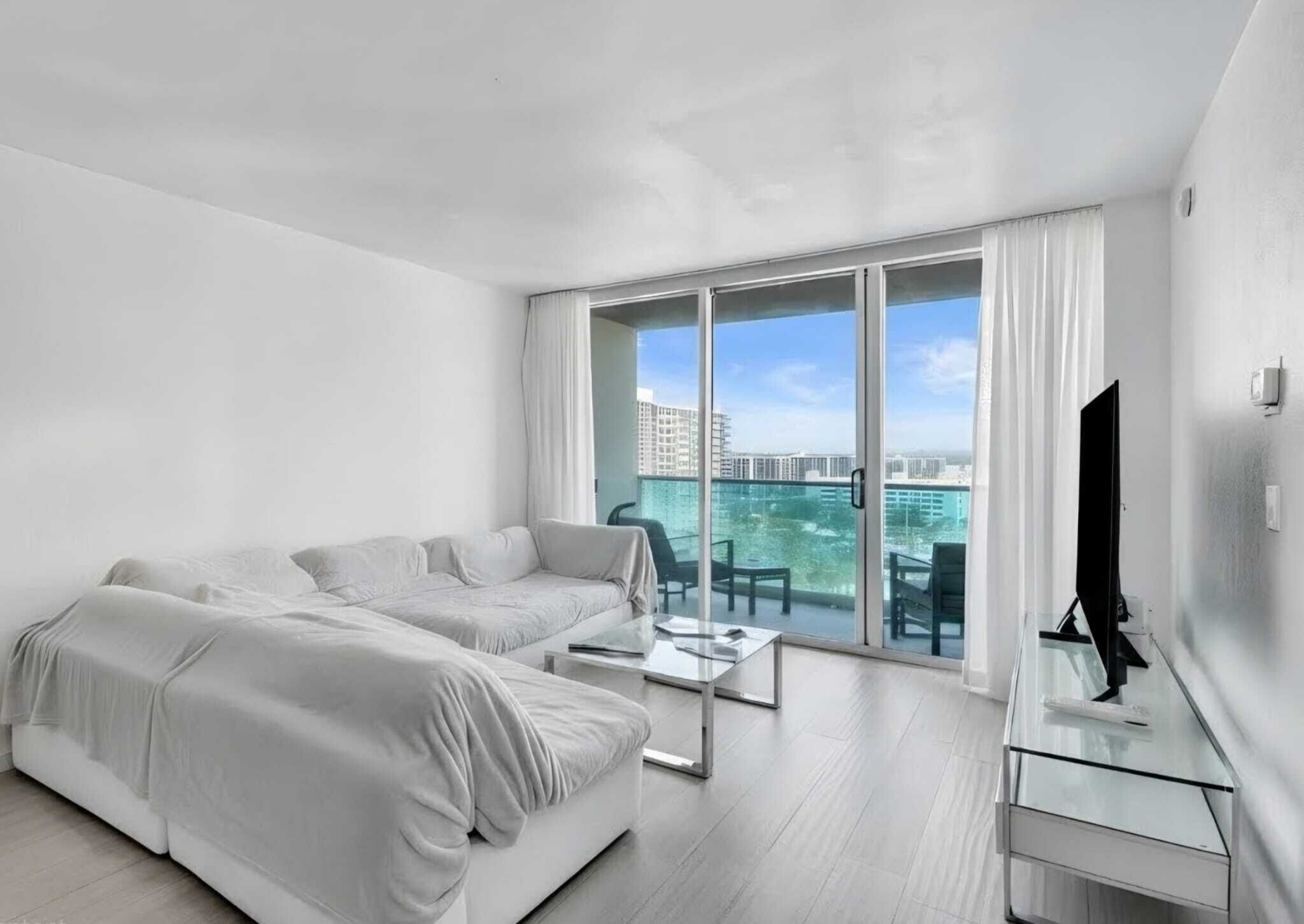 A modern hotel room with a large balcony, two beds, a glass table, and a TV.