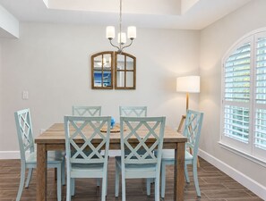 A dining area with a wooden table, six chairs, a chandelier, and a window with blinds. - 3BR Pool & Hot Tub Villa in Rotonda West (Rotonda West)