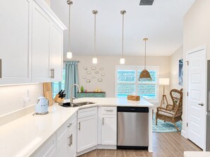 A modern kitchen with white cabinets, a stainless steel dishwasher, pendant lights, and a window with blinds. - 3BR Pool & Hot Tub Villa in Rotonda West (Rotonda West)