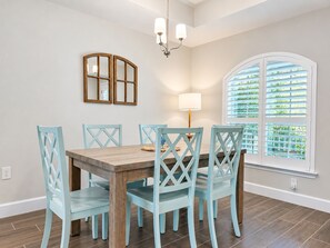 Un comedor con una mesa de madera y sillas azul claro, un candelabro y una ventana con contraventanas.