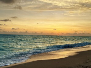 A beach with waves, a sunset, and a distant horizon.