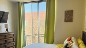 A hotel room with a bed, a dresser, a television, and a view of the outdoors.