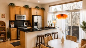 A modern kitchen with wooden cabinets, a central island, bar stools, and a dining table with chairs.