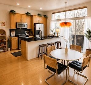 A modern kitchen with wooden cabinets, a central island, bar stools, and a dining table with chairs.