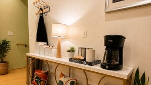 A modern living room with a wooden floor, a white console table, a coffee maker, a lamp, and decorative pillows.