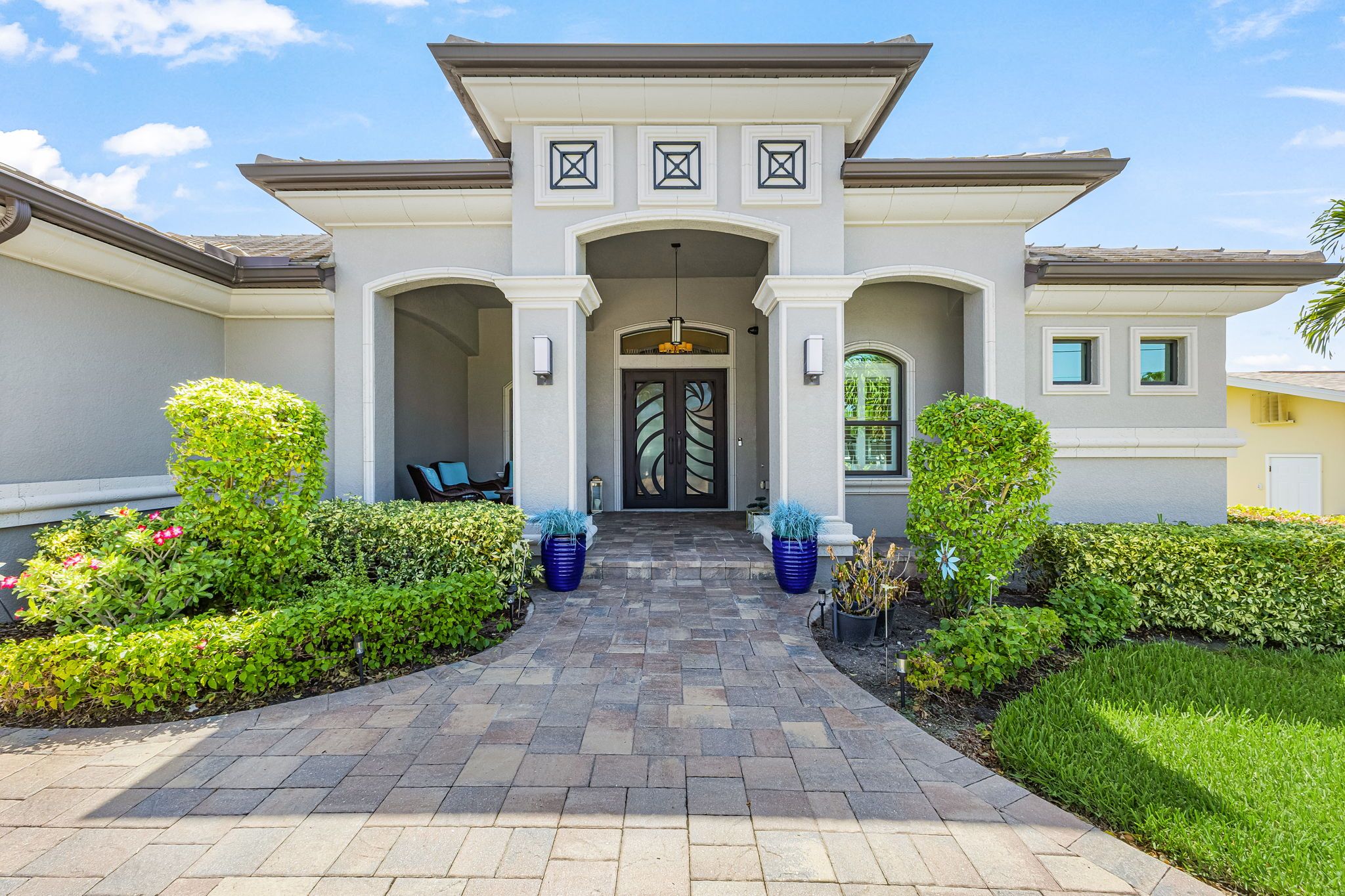 A modern entrance with a central archway, flanked by symmetrical landscaping and a paved walkway.