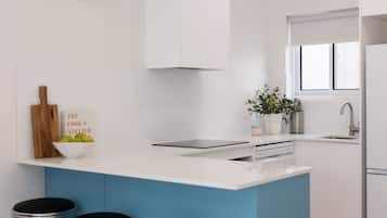 A modern kitchen with a white and blue color scheme, a built-in island with bar stools, a clock on the wall, and a window providing natural light.