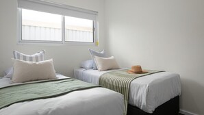 Ein Zimmer mit zwei Betten, einem Fenster mit Jalousien und einem Hut auf einem Bett.