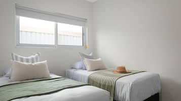 A room with two beds, a window with blinds, and a hat on one bed.