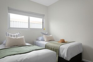 Quarto com duas camas, uma janela com persianas e um chapéu sobre uma das camas.