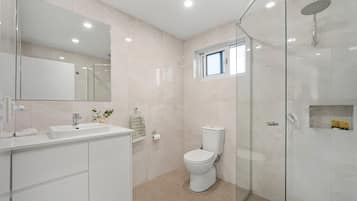 A modern bathroom with a glass shower enclosure, a toilet, a sink with a mirror, and a small window above the toilet.