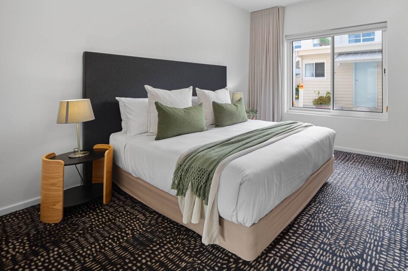 A hotel room with a bed, two bedside tables, a window, and patterned carpet.