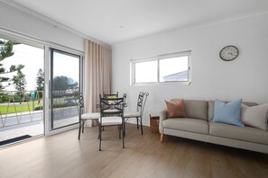 Ein stilvolles Wohnzimmer mit einer Couch, einem Esstisch mit Stühlen, einem großen Fenster und einer Wanduhr.