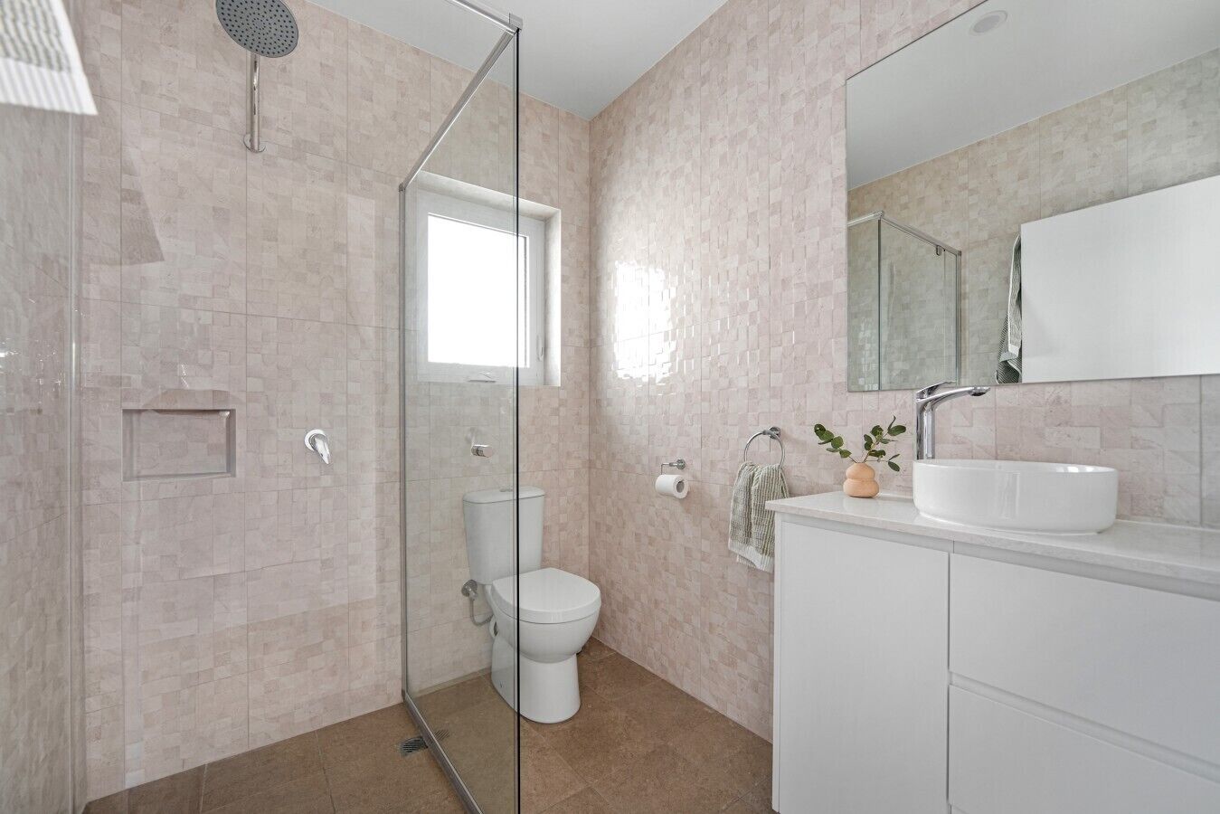 A modern bathroom with a glass shower enclosure, a toilet, a sink with a mirror, and a potted plant.