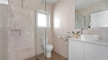 A modern bathroom with a glass shower enclosure, a toilet, a sink with a mirror, and a potted plant.