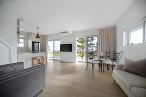 Un salon moderne comprenant un canapé, une table à manger et des chaises, un coin cuisine avec un téléviseur, et un balcon avec vue.