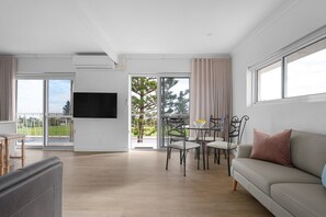 Ein modernes Wohnzimmer mit einer Couch, einem Esstisch mit Stühlen, einem flachbildfernseher an der Wand und einer großen Glastür, die auf einen Balkon führt.