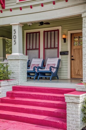 A porch with two blue chairs, a wooden door, and a number '505' on a column. - NEW Sisters on Alamo - Walk to Downtown Brenham! - Two Charming Cottages (Brenham)