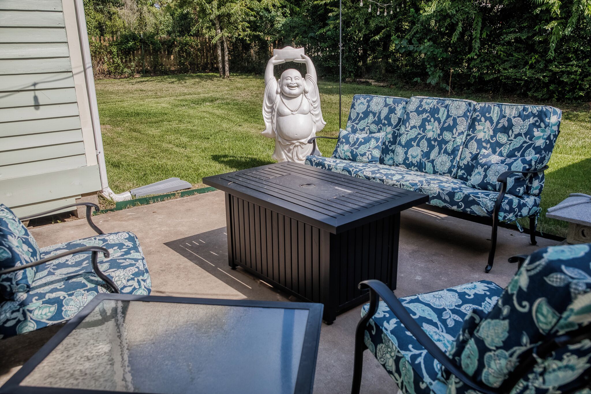 Un espace patio comprenant une table noire, deux chaises à motifs, un canapé et une statue décorative.