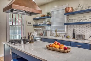 A modern kitchen with a copper range hood, blue cabinets, and a marble countertop.