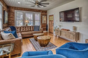 A living room with a brown leather sofa, two round wooden coffee tables, a blue armchair, and a wooden cabinet with decorative items.