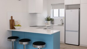Una cucina moderna con un'isola blu, mobili bianchi, un frigorifero in acciaio inossidabile, una sveglia e una pianta in vaso.