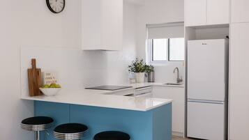 A modern kitchen with a blue island, white cabinets, a stainless steel refrigerator, a clock, and a potted plant.