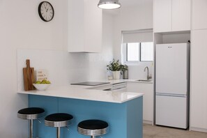 Eine moderne Küche mit einer blauen Kochinsel, weißen Schränken, einem Edelstahl-Kühlschrank, einer Uhr und einem Blumentopf.