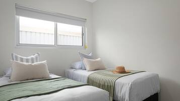A room with two beds, a window with blinds, and a hat on one bed.