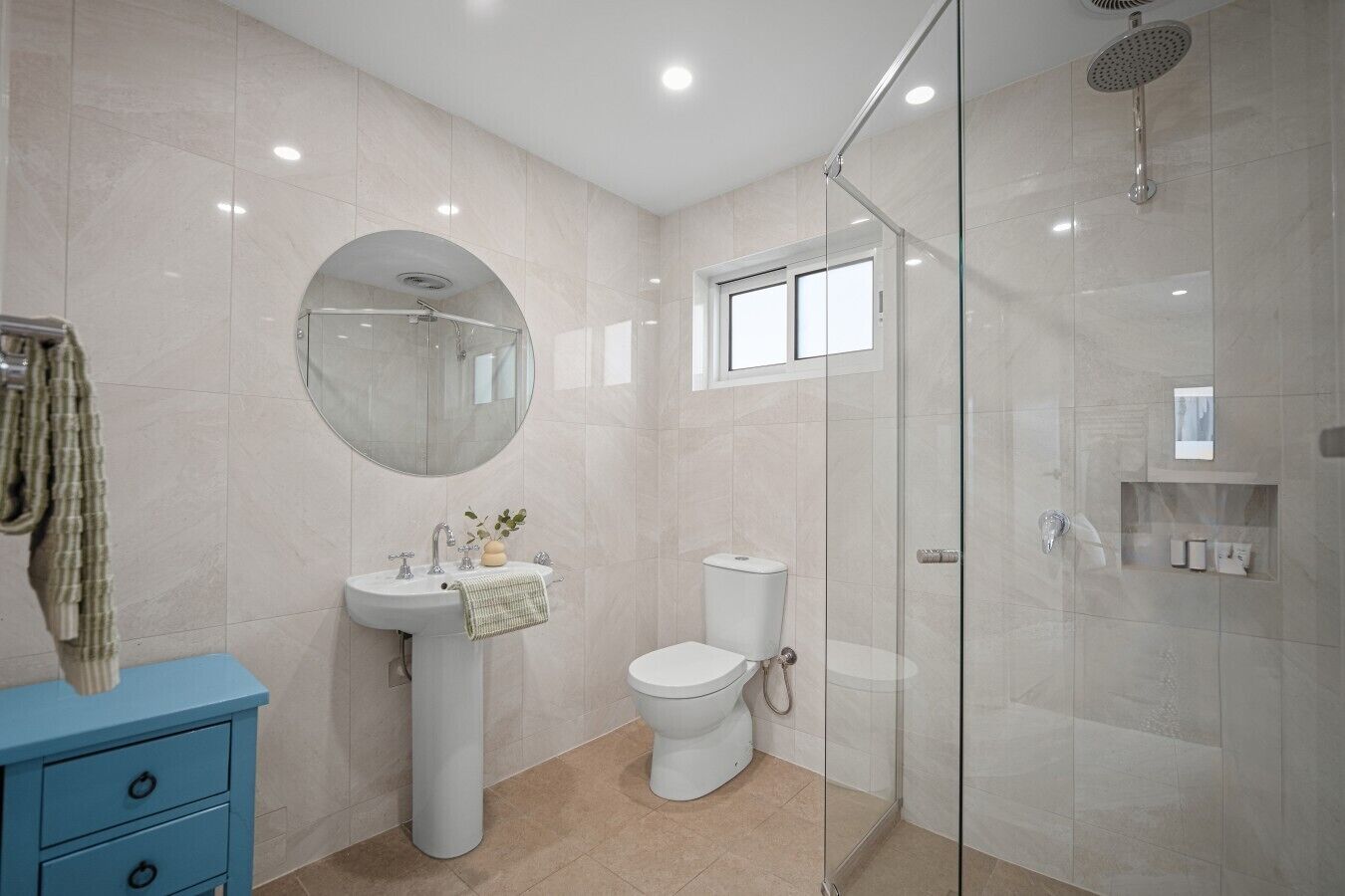 Une salle de bain moderne avec une douche à parois de verre, un miroir rond, un lavabo sur colonne et des toilettes.