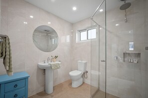 Ein modernes Badezimmer mit Duschkabine aus Glas, einem runden Spiegel, einem Standwaschbecken und einer Toilette.
