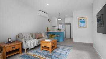 A modern living room with a sofa, coffee table, and a kitchen area in the background.