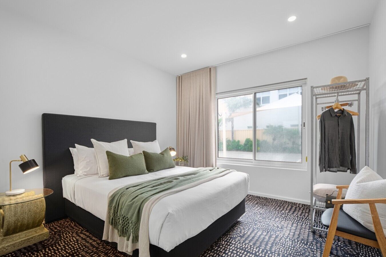 A modern hotel room with a large bed, bedside lamps, a window with a view, and a chair.