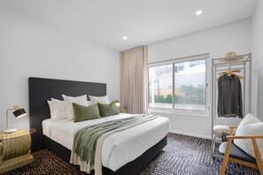 Ein modernes Hotelzimmer mit einem großen Bett, Nachttischlampen, einem Fenster mit Blick und einem Sessel.