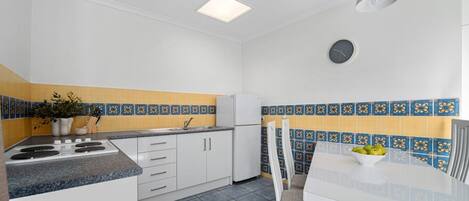 A compact kitchen with white cabinets, a granite countertop, a white dining table, and a blue and yellow patterned backsplash.