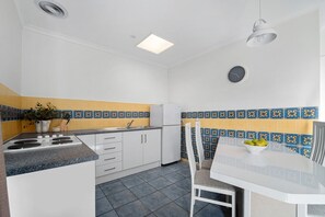Cocina compacta con armarios blancos, encimera de granito, mesa de comedor blanca y salpicadero con estampado azul y amarillo.