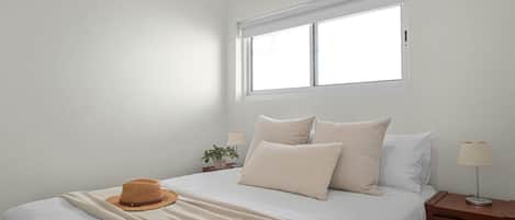 A bedroom with a bed, a window, an air conditioner, a nightstand, and a lamp.