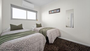 Ein Hotelzimmer mit zwei Betten, einem Fenster, einer Klimaanlage, einem gerahmten Bild und einem Spiegel.