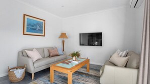 Ein Wohnzimmer mit einer Couch, einem Couchtisch, einem Fernseher und einem Bild an der Wand.