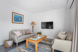 Ein Wohnzimmer mit einer Couch, einem Couchtisch, einem Fernseher und einem Bild an der Wand.