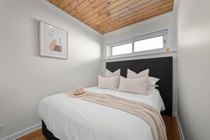 A bedroom with a bed, a window, a wooden ceiling, and a framed picture on the wall. - Esplanade Apartments | Ocean View Beachfront | West Beach (West Beach)