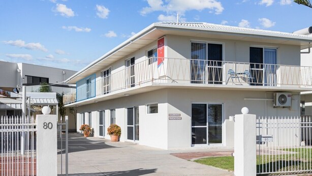 Um edifício moderno com entrada gradeada, número 80, e uma varanda com guarda-corpo.