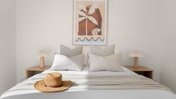 A bed with a straw hat, two bedside tables with lamps, and a framed picture on the wall.